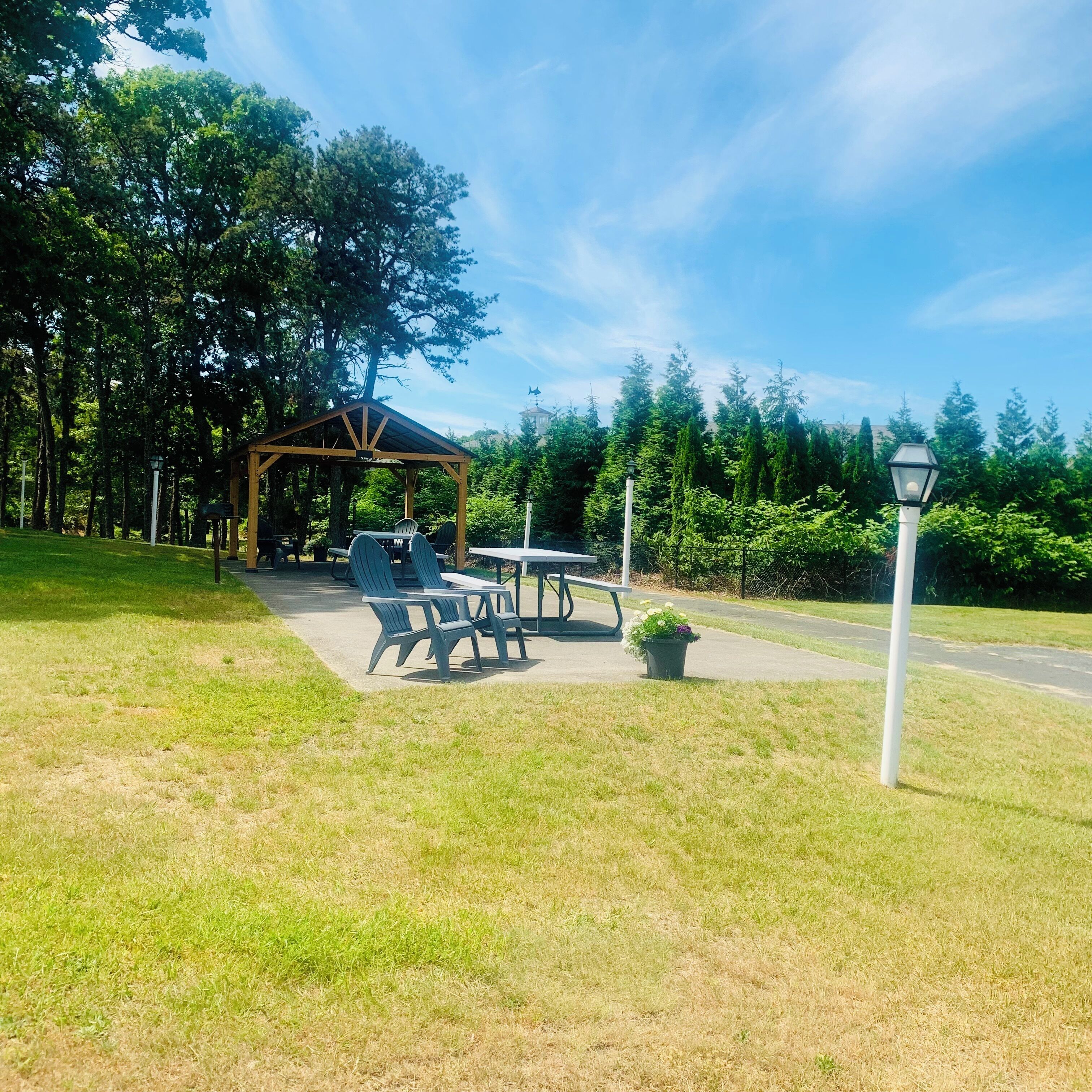 A gazebo with outdoor seating, surrounded by trees and a clear sky.