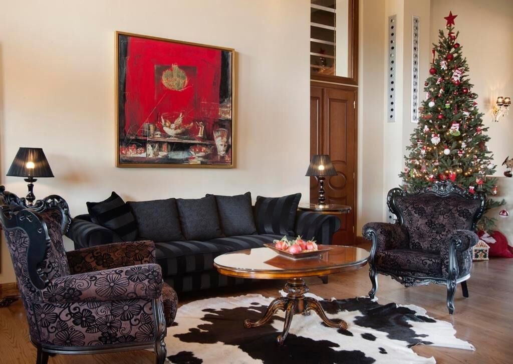 A living room with a black sofa, patterned armchairs, a glass coffee table, and a Christmas tree.