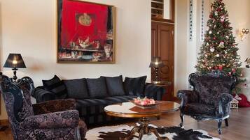 A living room with a black sofa, patterned armchairs, a glass coffee table, and a Christmas tree.