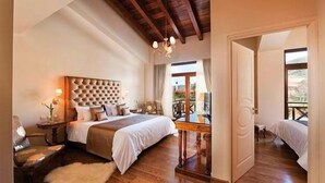 Un dormitorio con una cama grande, suelo de madera, un candelabro y vistas a través de una ventana.