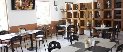 A restaurant with multiple tables and chairs, a television mounted on the wall, and shelves with decorative items.