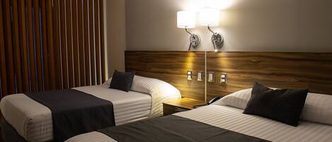 Habitación de hotel con dos camas, cabecera de madera, mesita de noche con lámpara y teléfono.