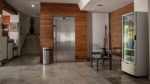 A lobby with a staircase, a trash bin, a vending machine, and a bench. - Estanza Hotel & Suites (Morelia)