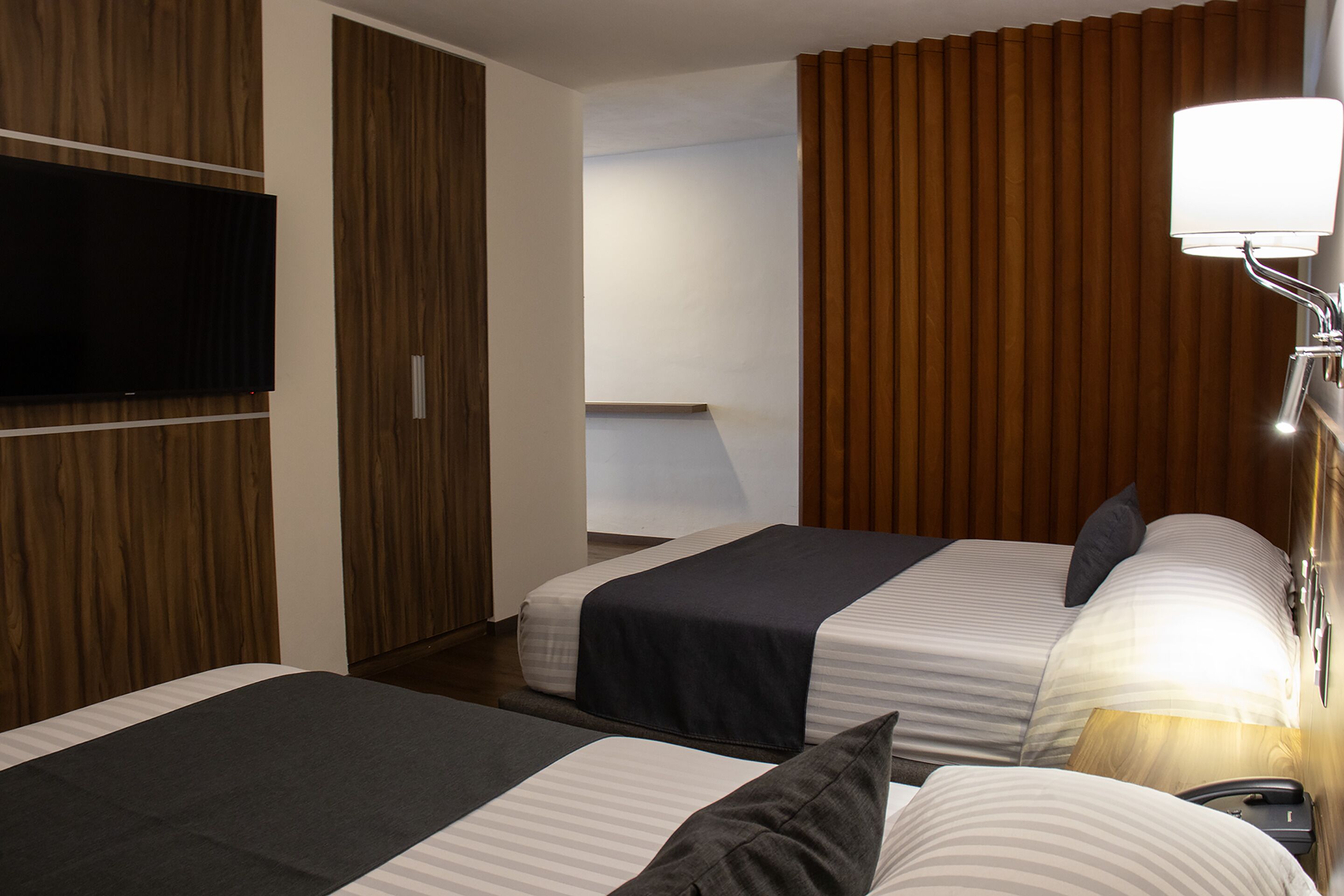 A hotel room with two beds, a TV mounted on the wall, and a bedside lamp.