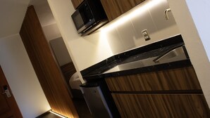 A modern kitchen with a microwave, stainless steel sink, and wooden cabinets. - Estanza Hotel & Suites (Morelia)