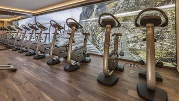 Varias bicicletas estáticas en un gimnasio con piso de madera y vista a un paisaje rocoso a través de un ventanal grande.
