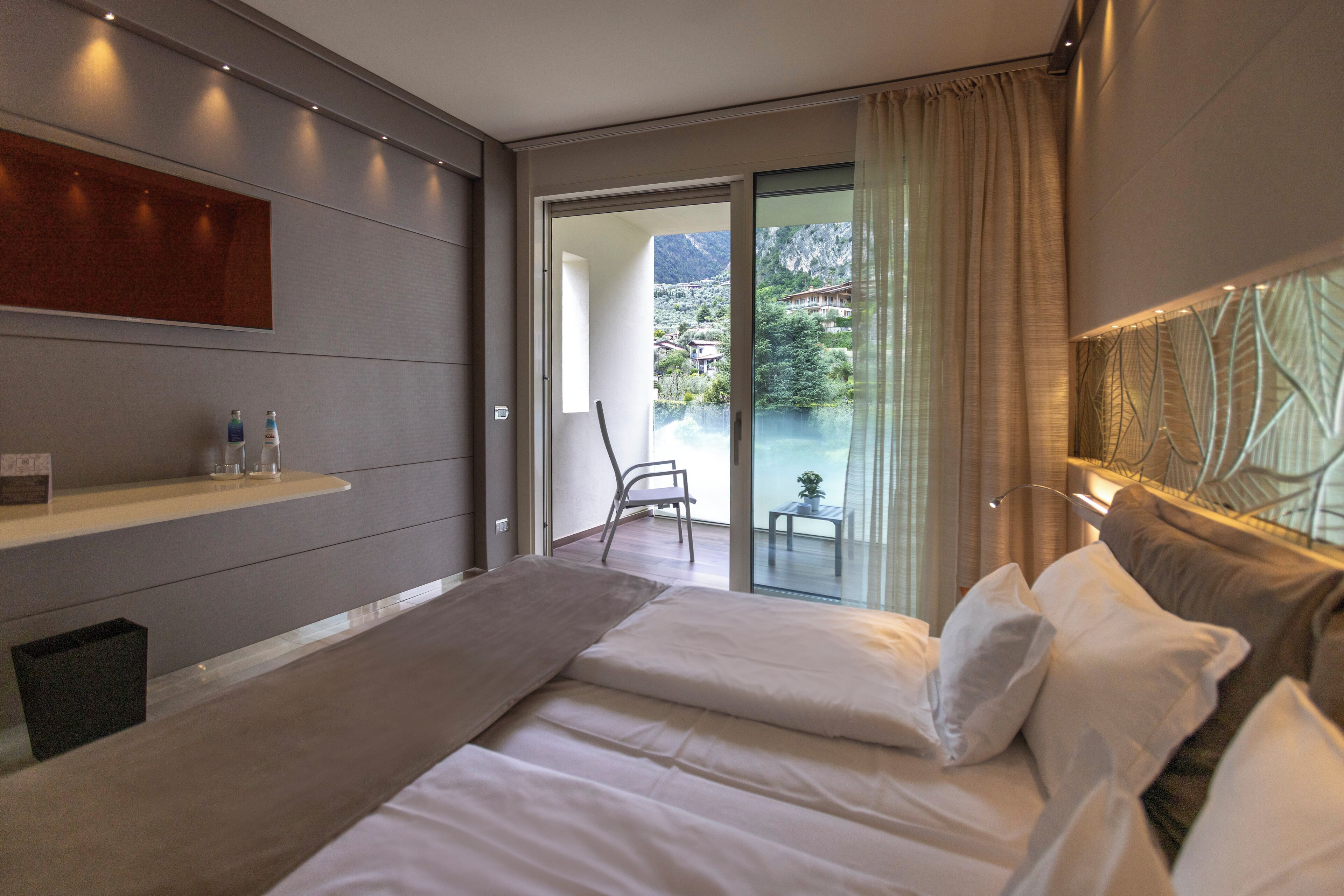 A modern hotel room with a large bed, a small table, and a view of a mountain landscape.