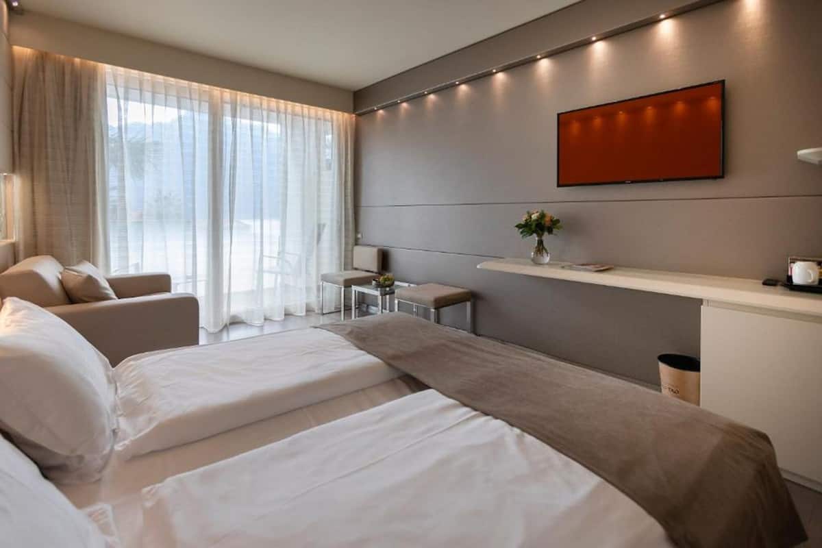 A hotel room with a bed, a sofa, a small table, a TV, and a window with curtains.