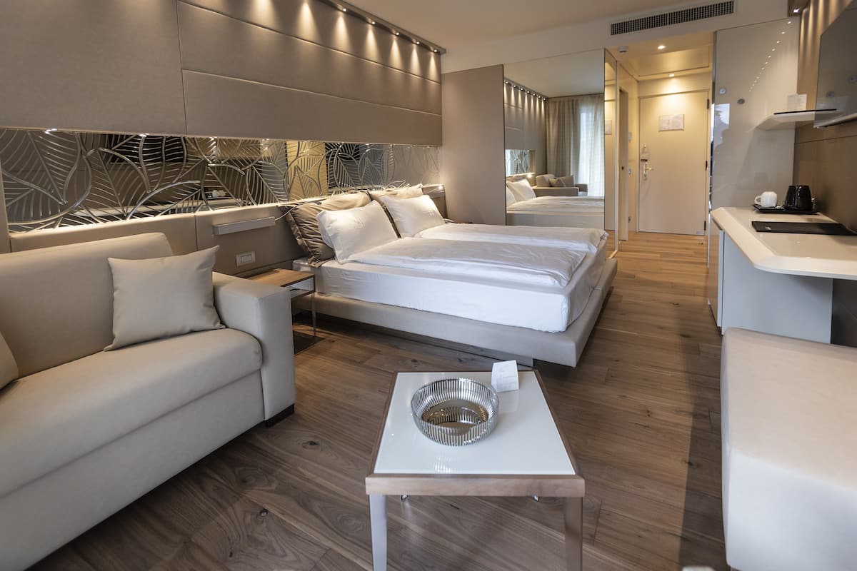 A modern hotel room with a large bed, a sofa, a small table with a decorative bowl, and a mirror.
