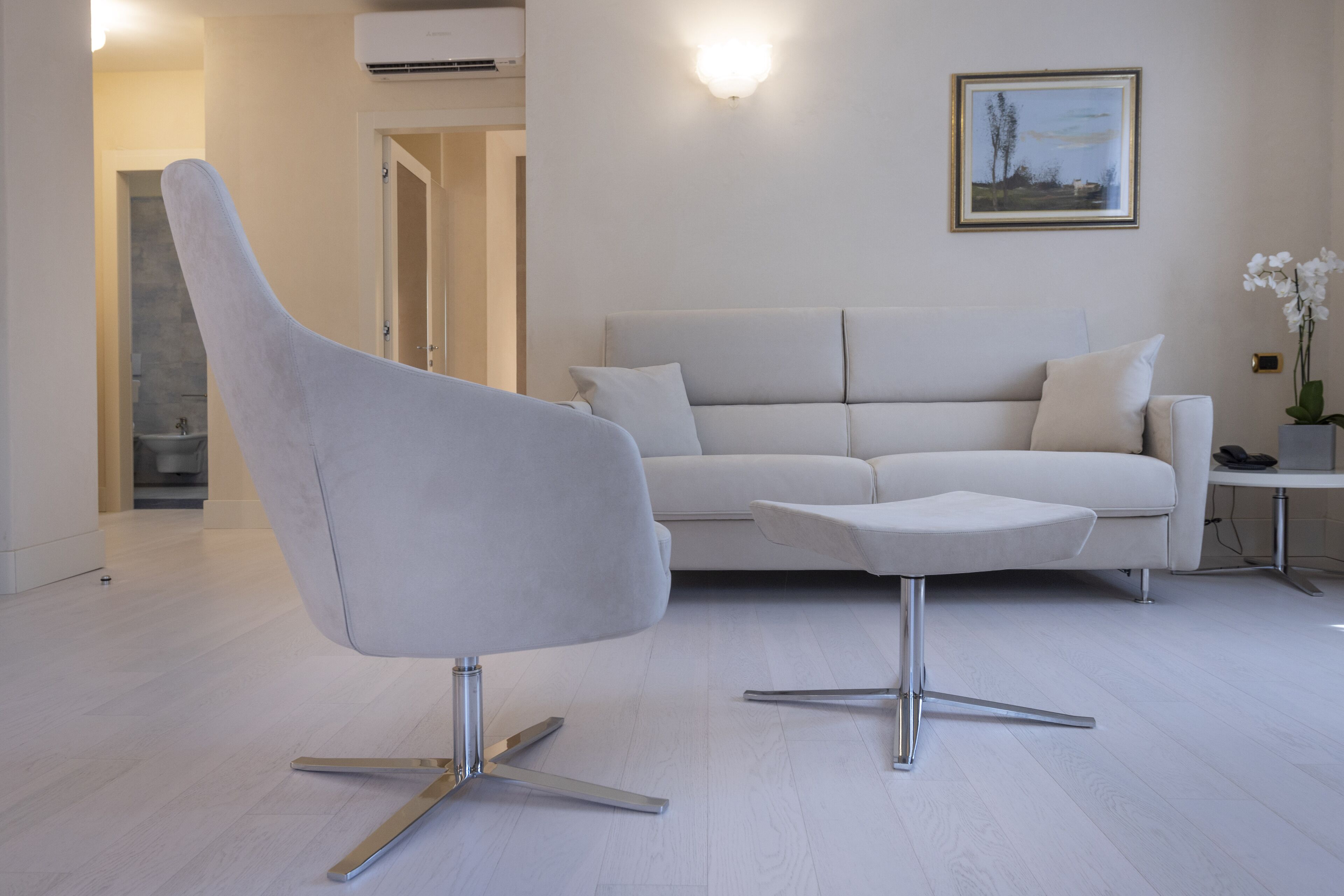 Ein modernes Wohnzimmer mit einem weißen Sofa, einem weißen Sessel und einem kleinen Beistelltisch mit einer Blumenvase.