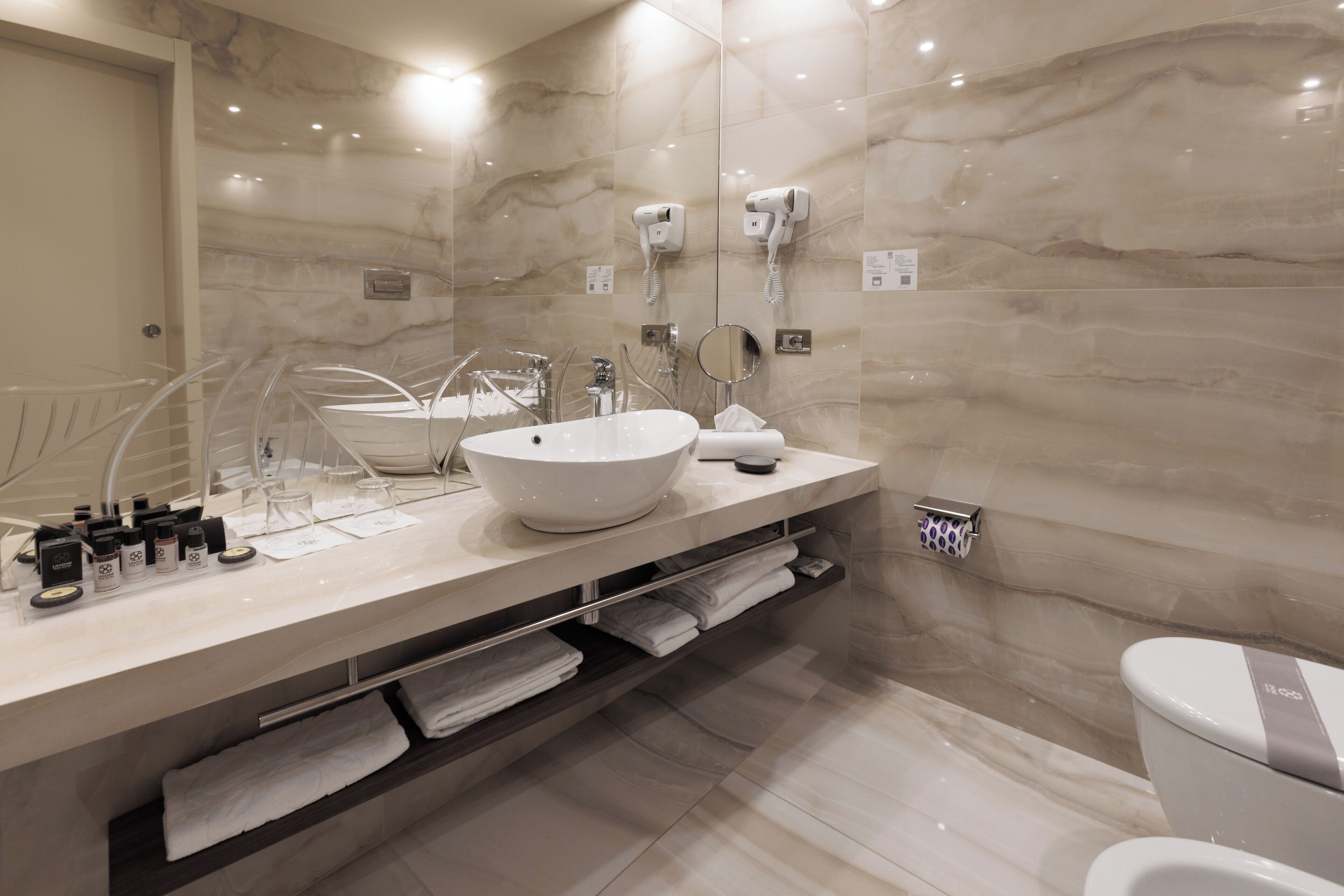 Un baño moderno con un lavabo blanco grande, un espejo y un inodoro. Hay toallas y artículos de aseo en la encimera.