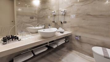 Un baño moderno con un lavabo blanco grande, un espejo y un inodoro. Hay toallas y artículos de aseo en la encimera.