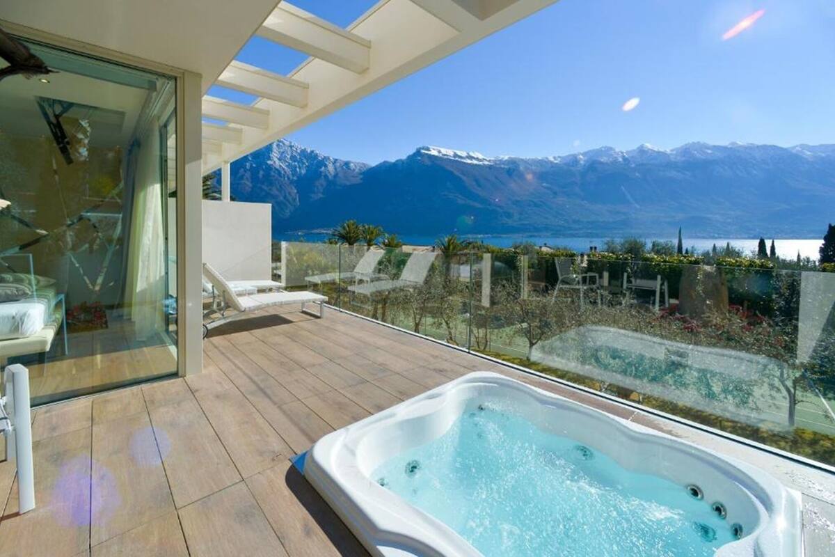 A balcony with a hot tub, lounge chairs, and a glass wall offering a mountain view.