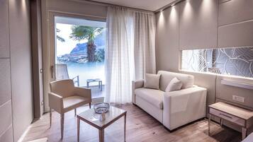 A modern living room with a sofa, armchair, and coffee table, a small side table, and a large window with a view of a palm tree and mountains.