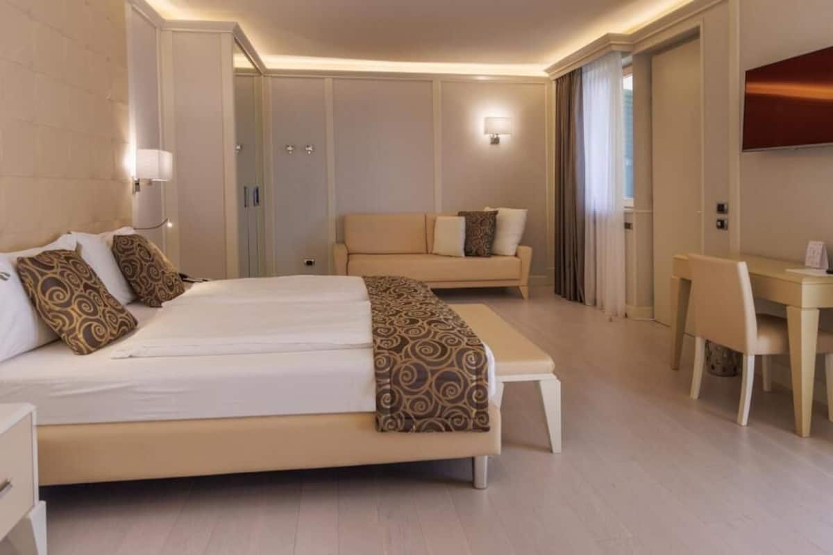 A modern hotel room with a large bed, a sofa, a desk, and a TV.