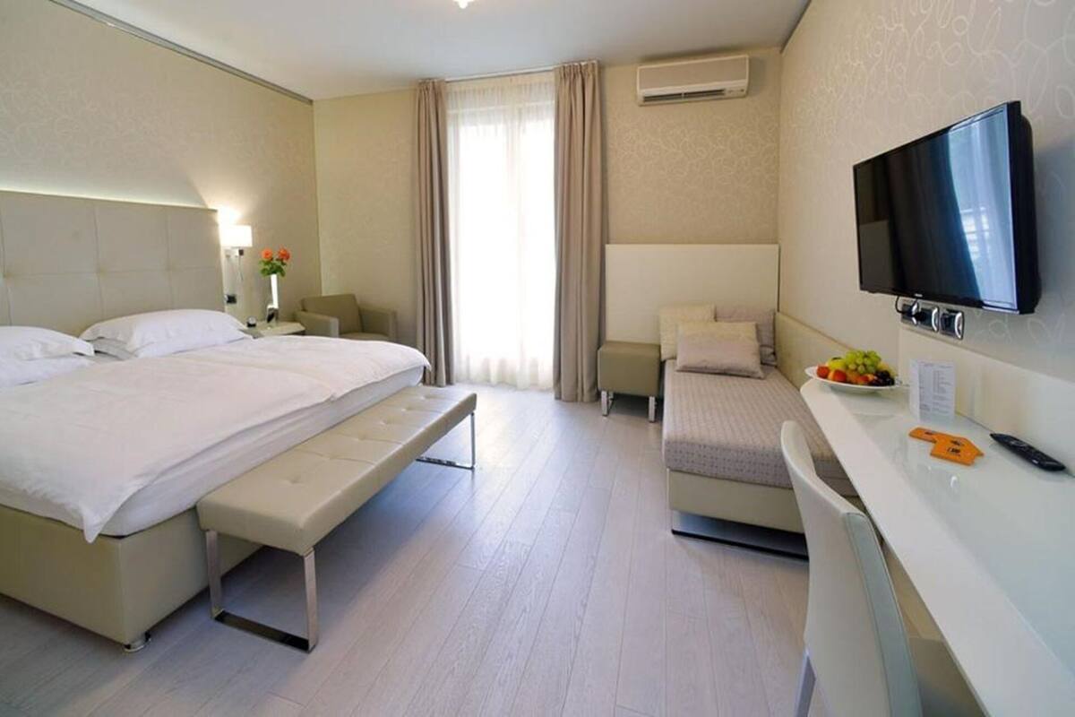 A hotel room with a large bed, a desk with a TV, and a small seating area.