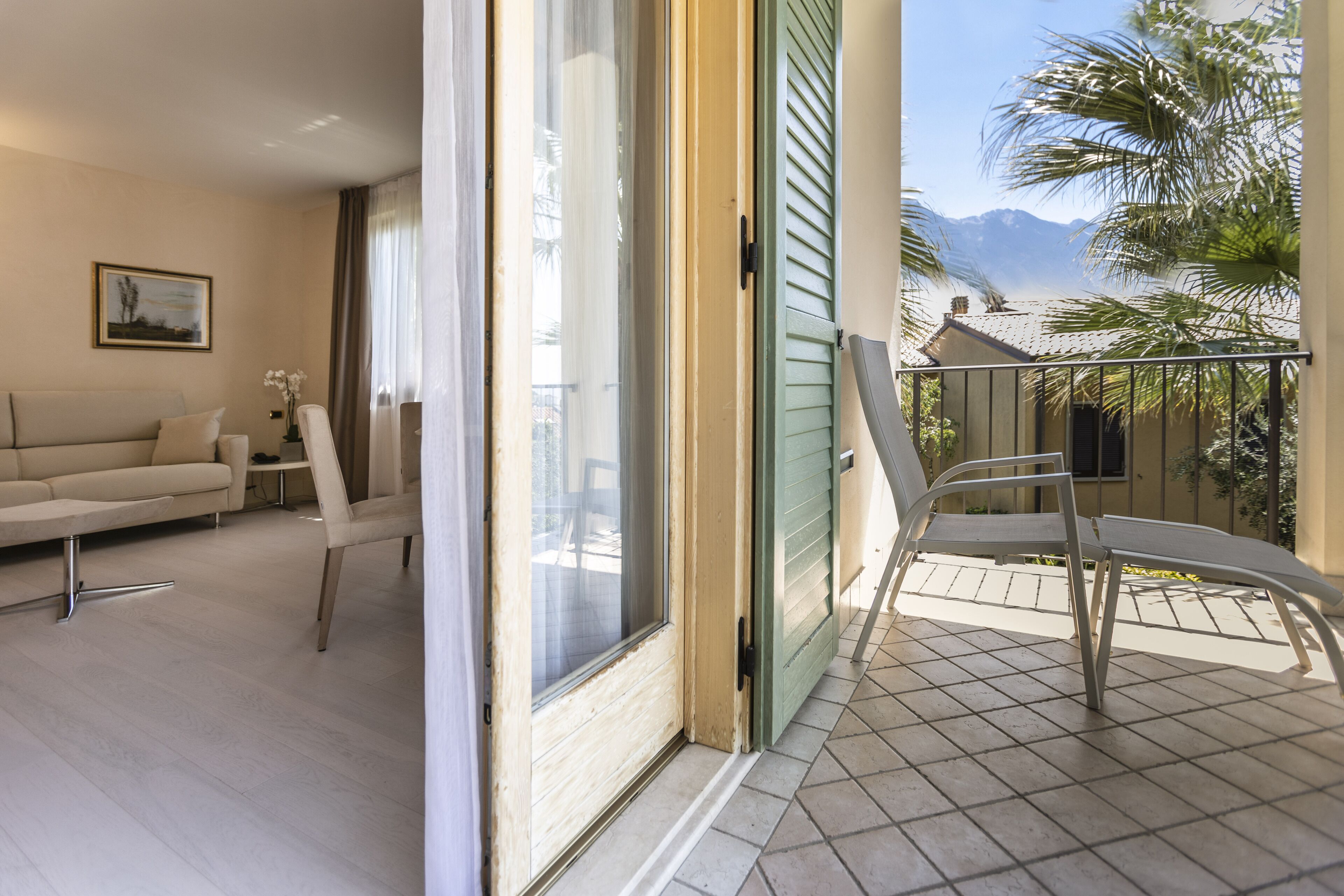 Ein Wohnzimmer mit einer Couch, Sesseln und einer Glasschiebetür, die auf einen Balkon mit Blick auf Palmen und Berge führt.