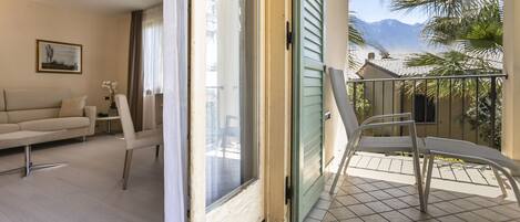 Sala de estar con sofá, sillas y puerta corrediza de vidrio que da a un balcón con vistas a palmeras y montañas.