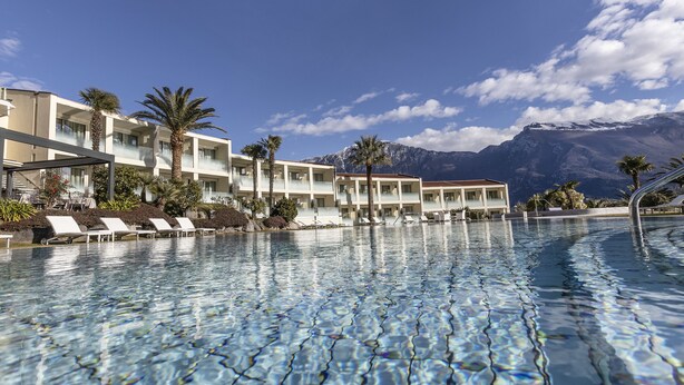 A hotel with a pool, palm trees, and mountains in the background. - Park Hotel Imperial Centro Tao Natural Medical Spa (Limone sul Garda)