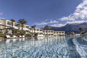 A hotel with a pool, palm trees, and mountains in the background.