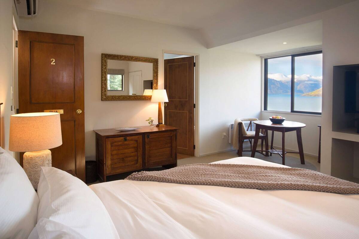 A hotel room with a bed, a desk, a chair, a lamp, a mirror, and a window with a view.