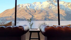 A room with a view of a mountain and a lake. There are two leather sofas and a small table with a vase of flowers. - Hidden Lodge Queenstown (Queenstown)