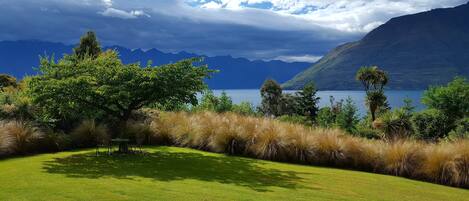 A grassy area with a table and chairs, surrounded by trees and a view of mountains and a lake.