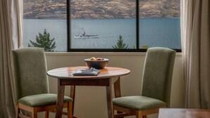 A room with a view of a lake and mountains. There is a table with a bowl and a book. Two chairs are placed around the table. - Hidden Lodge Queenstown (Queenstown)
