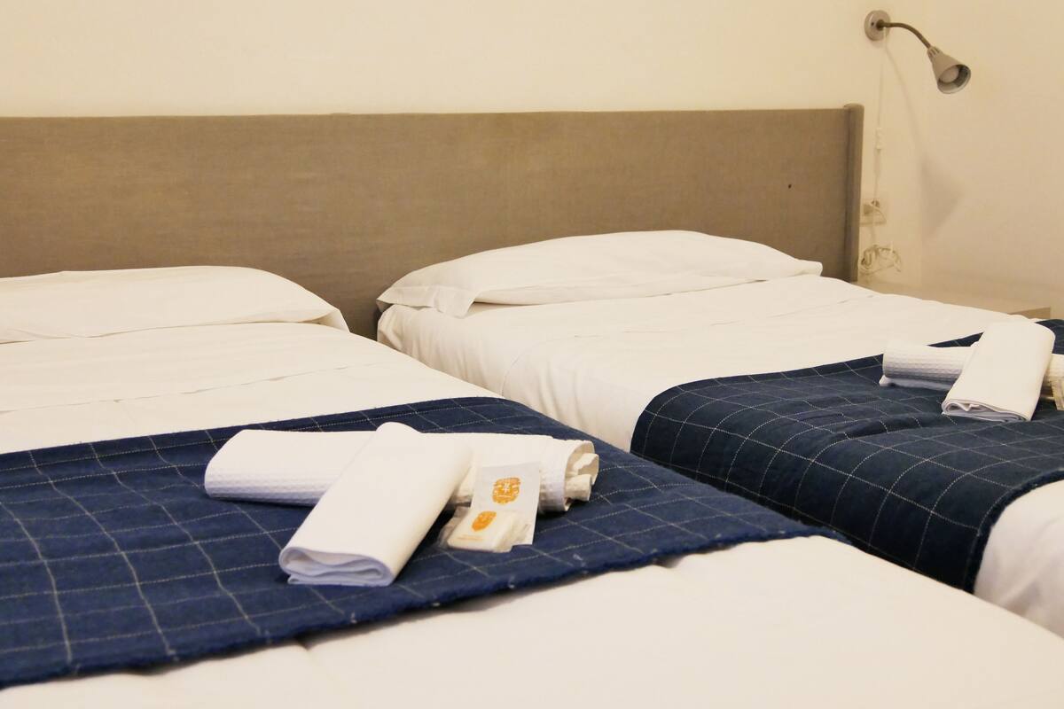 A hotel room with two single beds, each with a blue quilt and white linens.