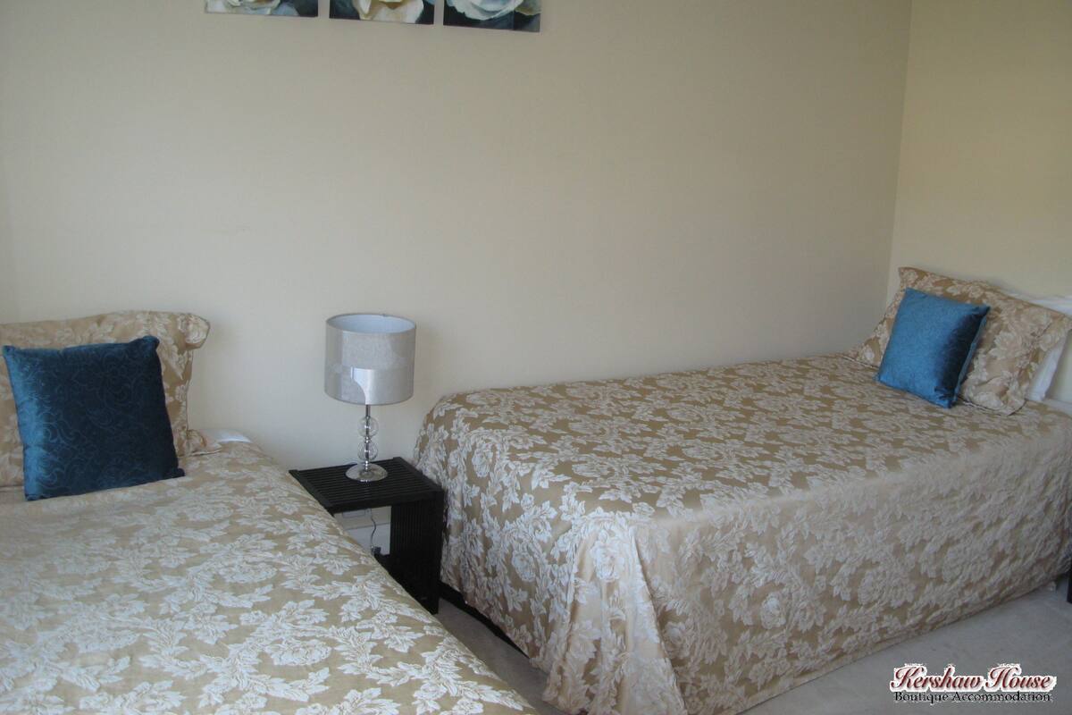 A hotel room with two beds, a nightstand with a lamp, and a floral painting on the wall.