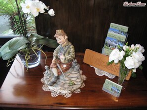 A wooden desk with a ceramic figurine of a man with a horse, a welcome sign, a framed brochure, and a vase with white flowers. - Kershaw House Boutique Accommodation (Richmond)
