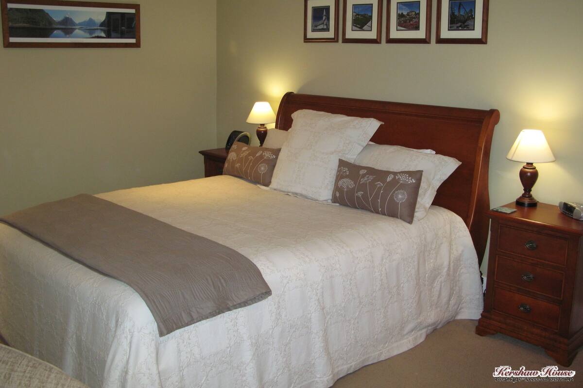 A neatly made bed with a brown throw blanket, a wooden headboard, and two bedside lamps. There are three framed pictures on the wall above the bed.