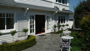 Una casa de dos pisos con un porche cubierto y un sendero de piedra que conduce a un espacio de estar exterior blanco.