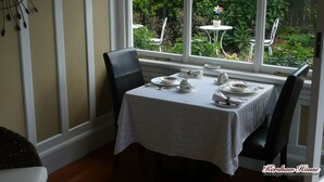 Un comedor con una mesa dispuesta para cuatro, una ventana que ofrece vistas a zonas verdes y una silla con cojín.