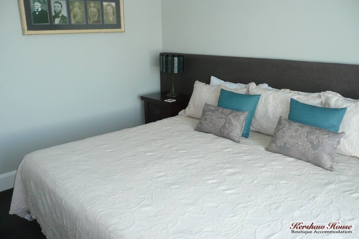 A neatly made bed with a white quilt, a dark headboard, and two decorative pillows.