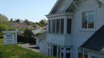 A white two-story house with a prominent bay window and a sign indicating it is a boutique accommodation.