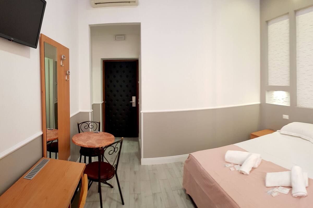 Ein Hotelzimmer mit Bett, Schreibtisch, Stuhl, einem kleinen Tisch und einem Spiegel.