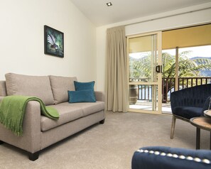 A living room with a beige sofa, blue cushions, a green throw, and a dark blue armchair.