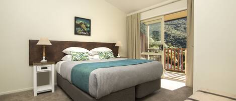 Un dormitorio con cama, mesitas de noche, un cuadro y un balcón con vistas a zonas verdes.