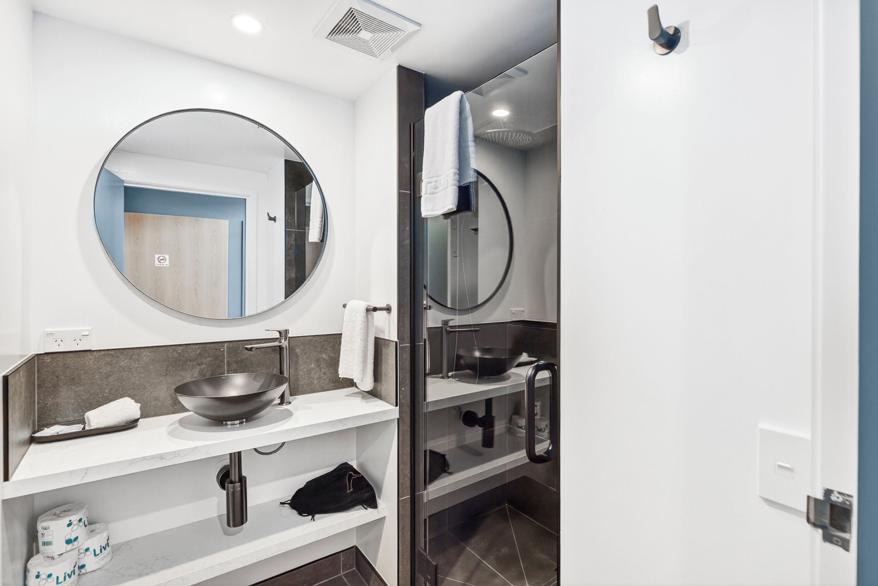 A modern bathroom with a round mirror, a sink with a bowl, a towel rack, and a shower area.