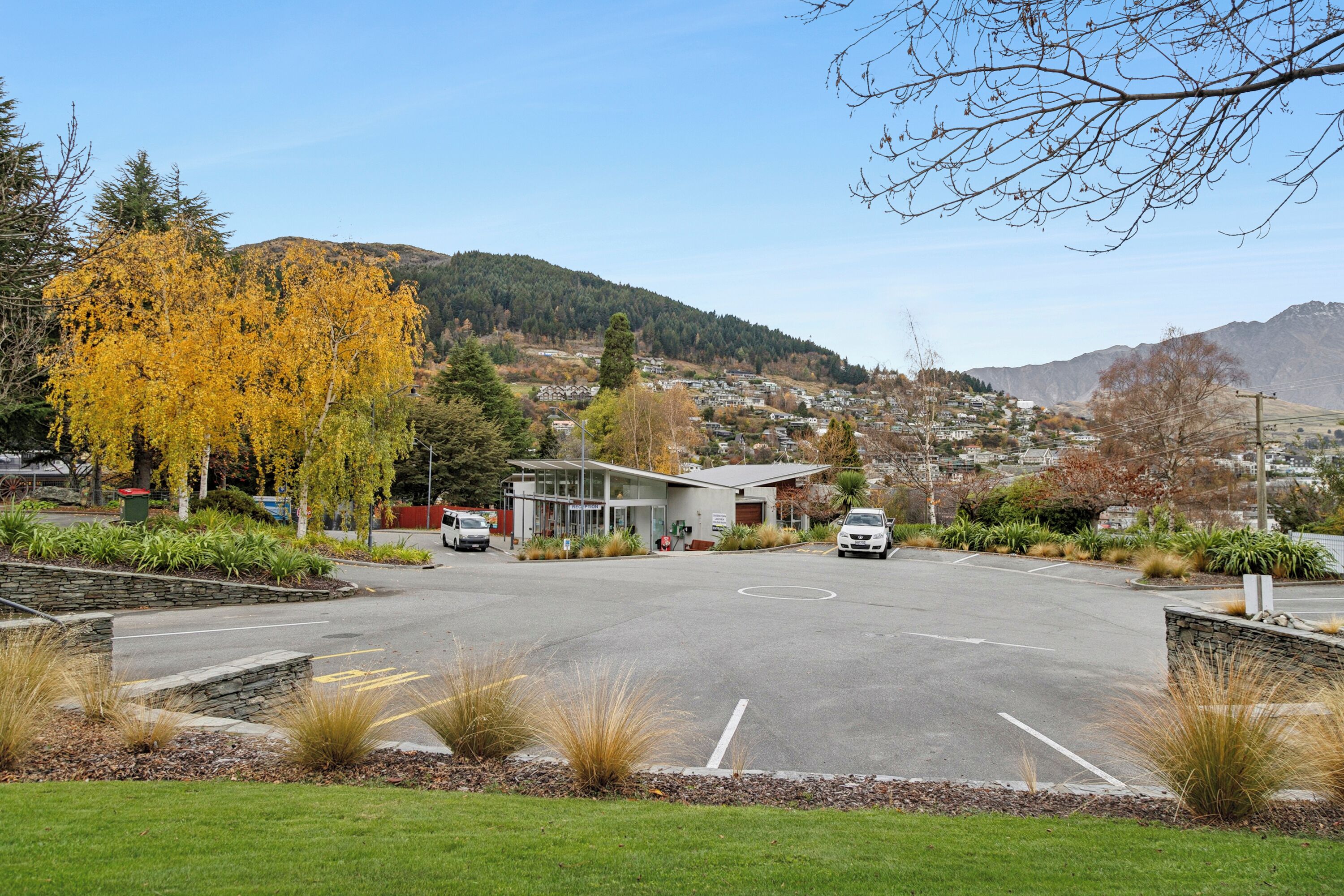 A parking lot with a building in the background, surrounded by trees and hills.