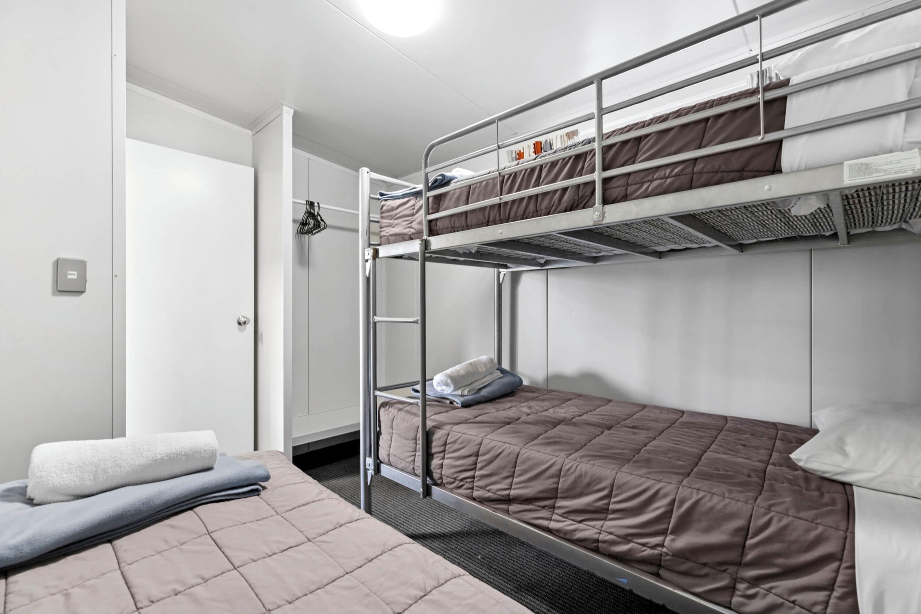 A bunk bed room with a ladder, a white door, and a small table with a towel.