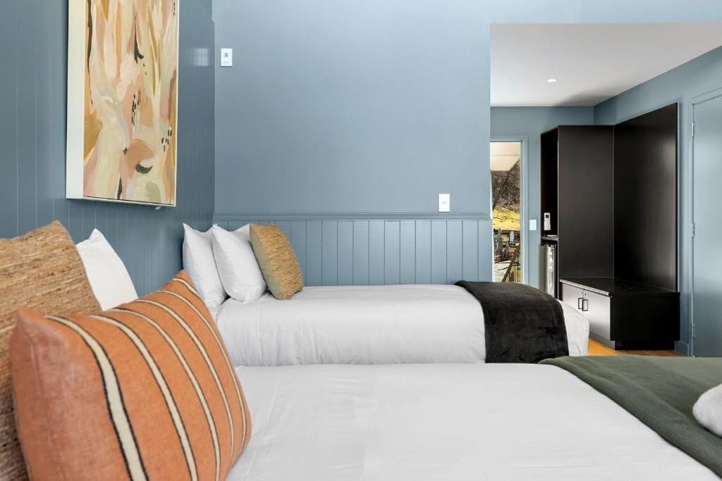 A hotel room with two beds, a large painting on the wall, and a television on the right.