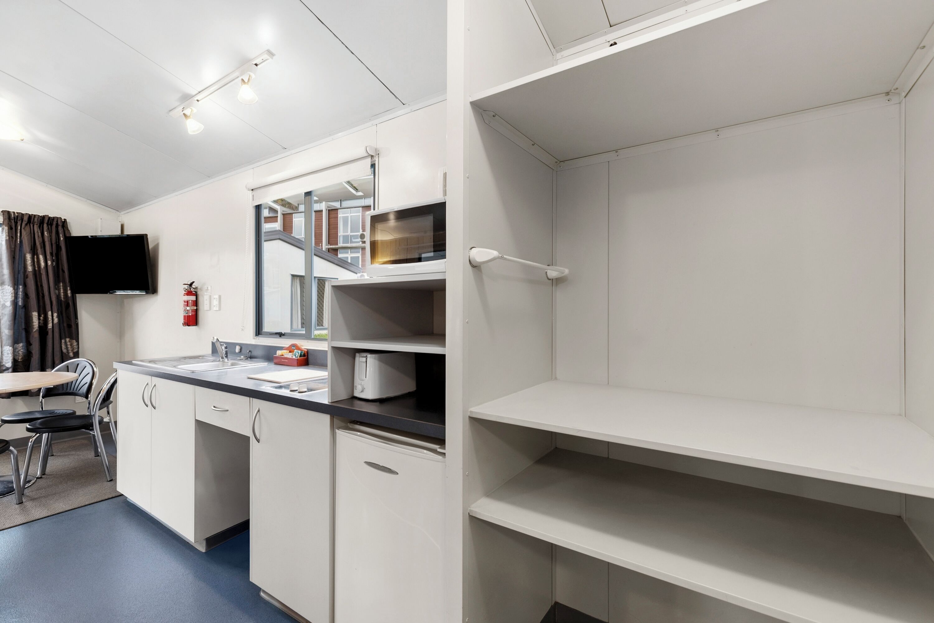 Een moderne keuken met witte kastjes, een ingebouwde magnetron en een flatscreen televisie aan de muur.