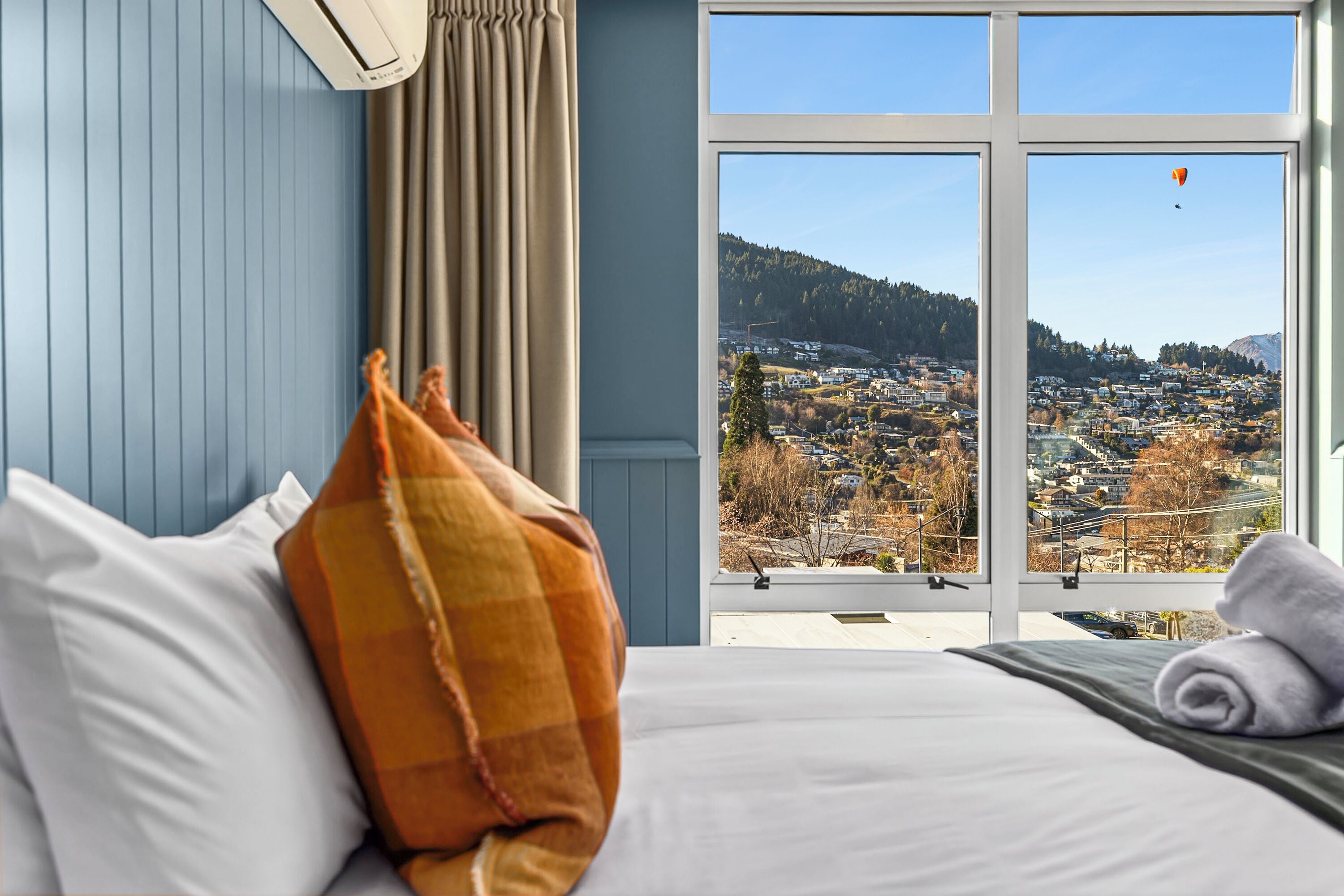 A bedroom with a large window offering a view of a town and hills.