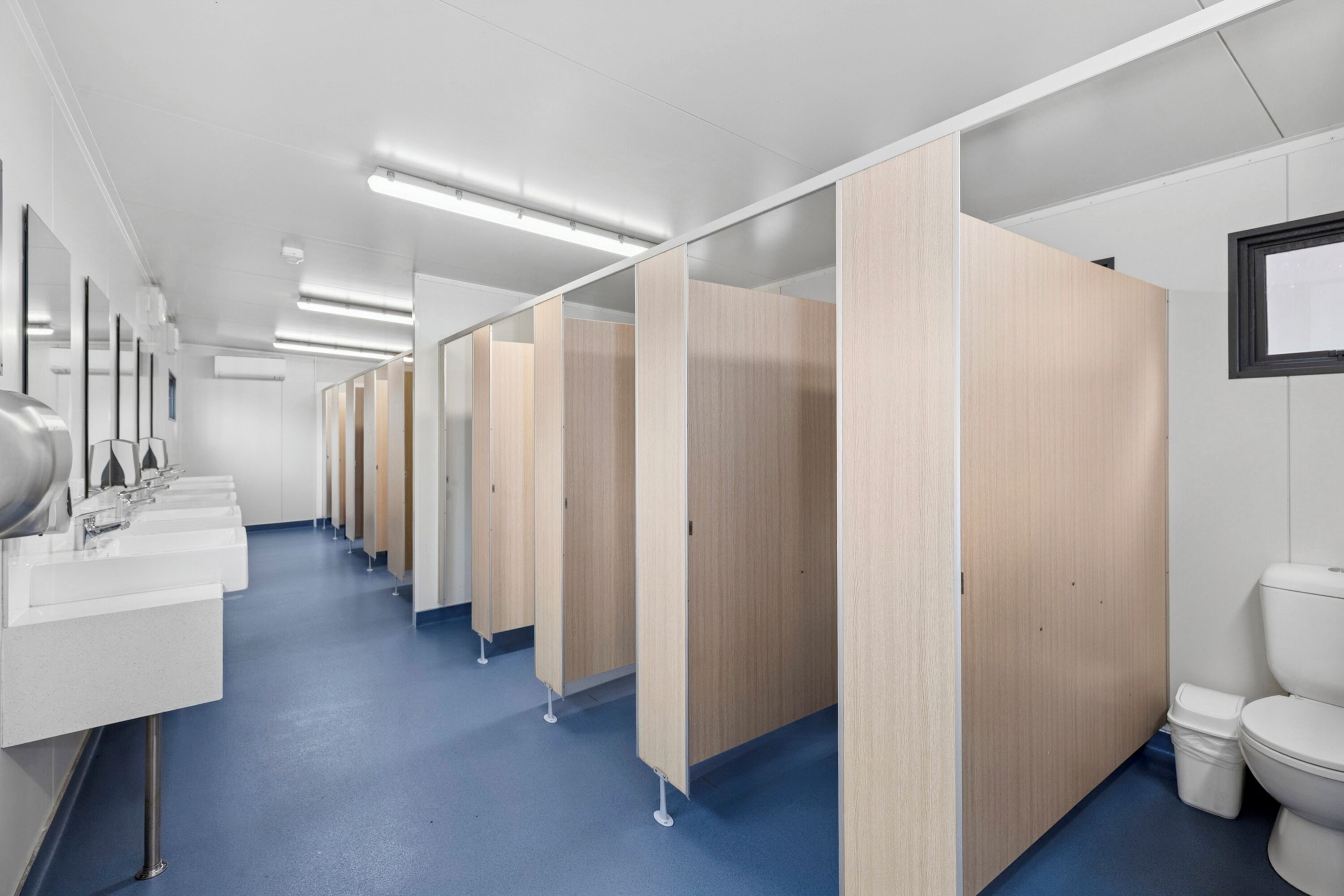 A public restroom with multiple sinks, wooden partitions, and a blue floor.