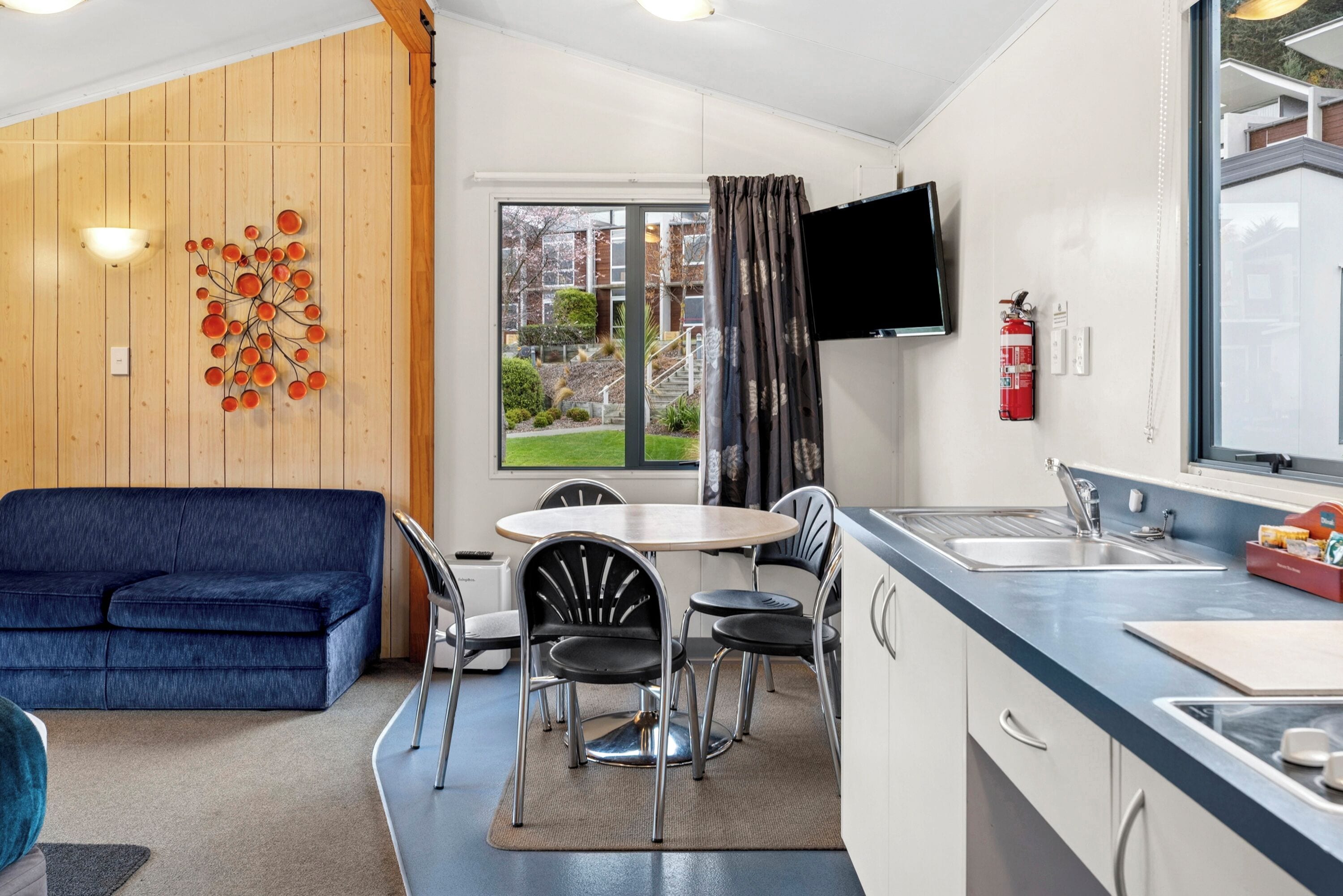Un espacio habitable compacto con sofá, mesa de comedor, sillas y área de cocina con lavamanos y televisor de pantalla plana.