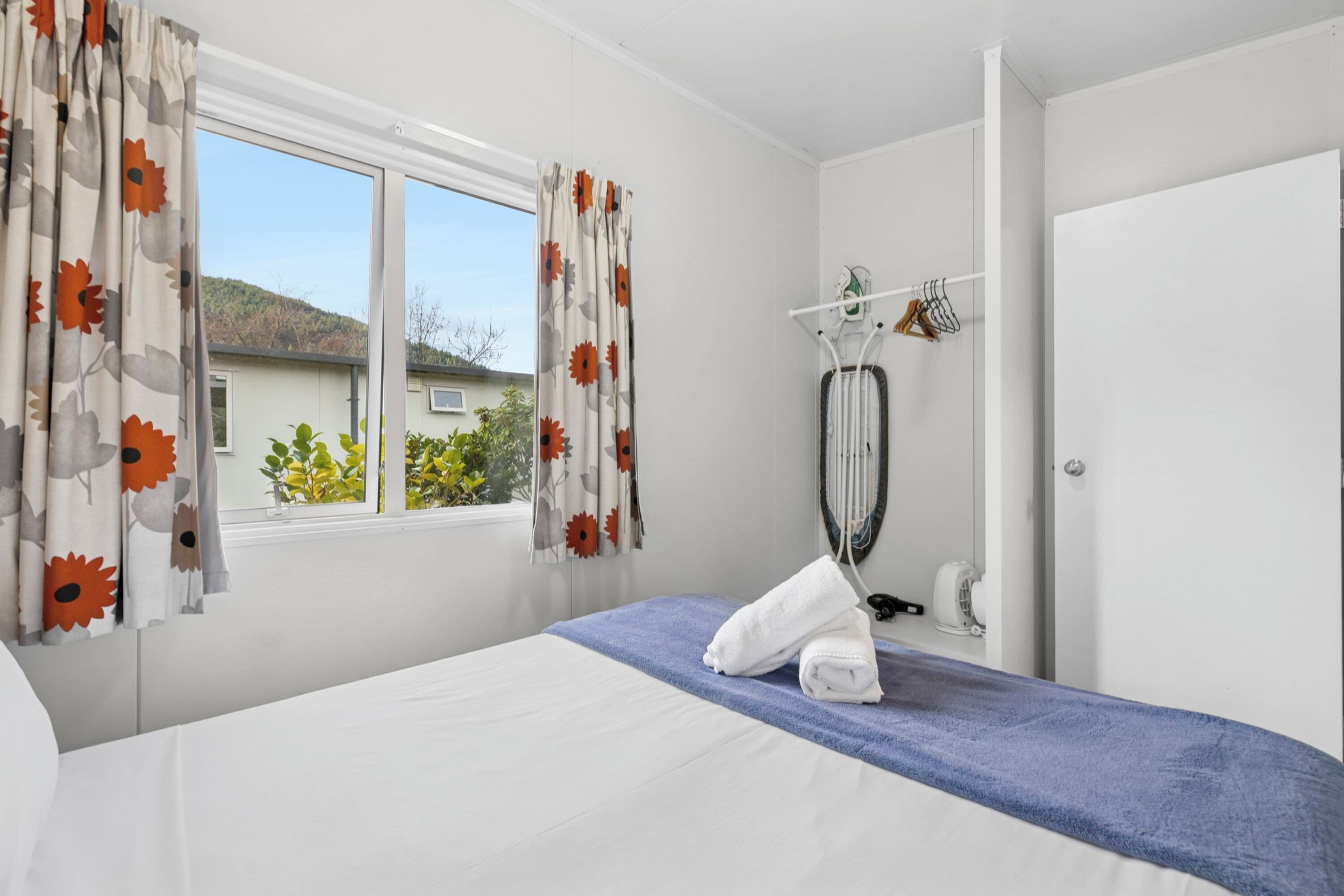 A hotel room with a bed, a window with curtains, a towel on the bed, a hairdryer, and a mirror.