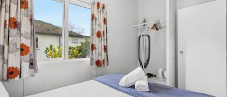 Quarto de hotel com cama, janela com cortinas, toalha sobre a cama, secador de cabelo e espelho.