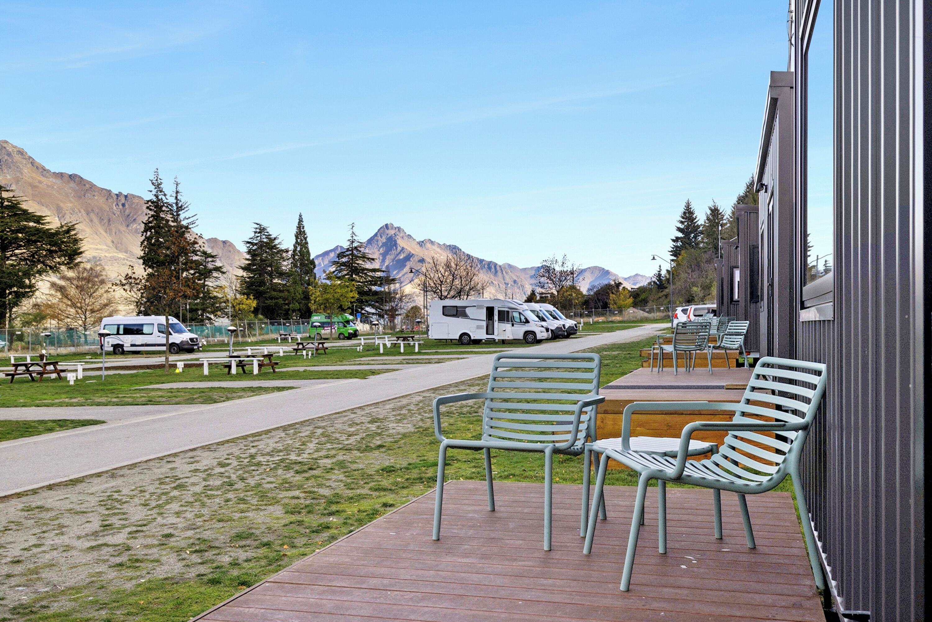 A deck with outdoor seating, a pathway, and a view of mountains and parked vehicles.